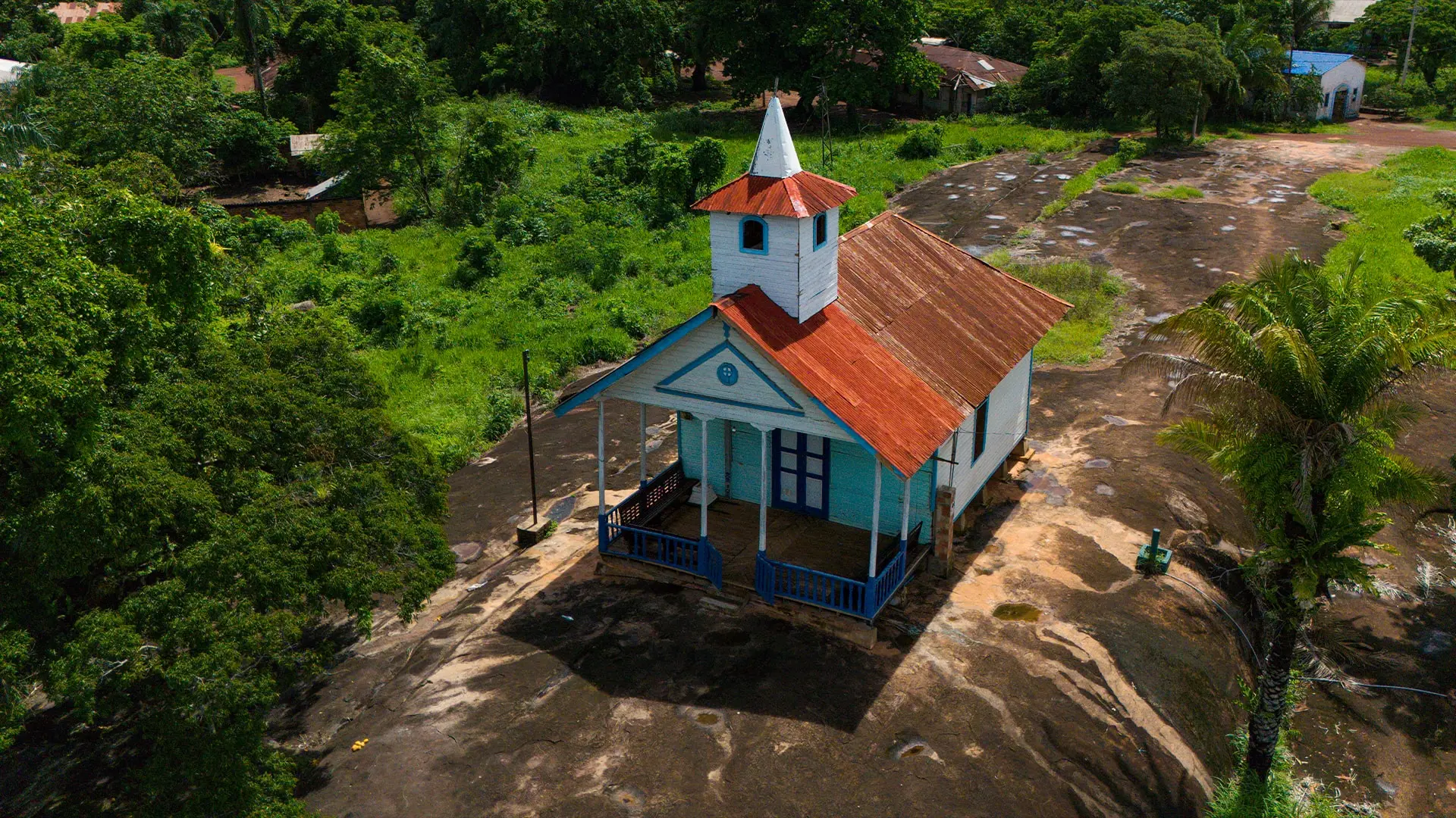 Vista aérea de una capilla celeste con techo rojo entre la selva