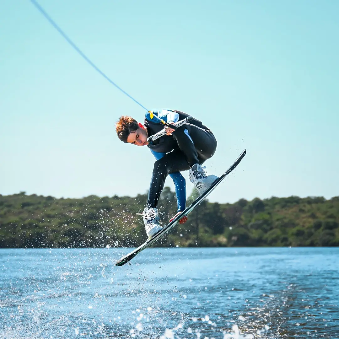 Wakeboarder girando sobre el agua con la orilla verde detrás