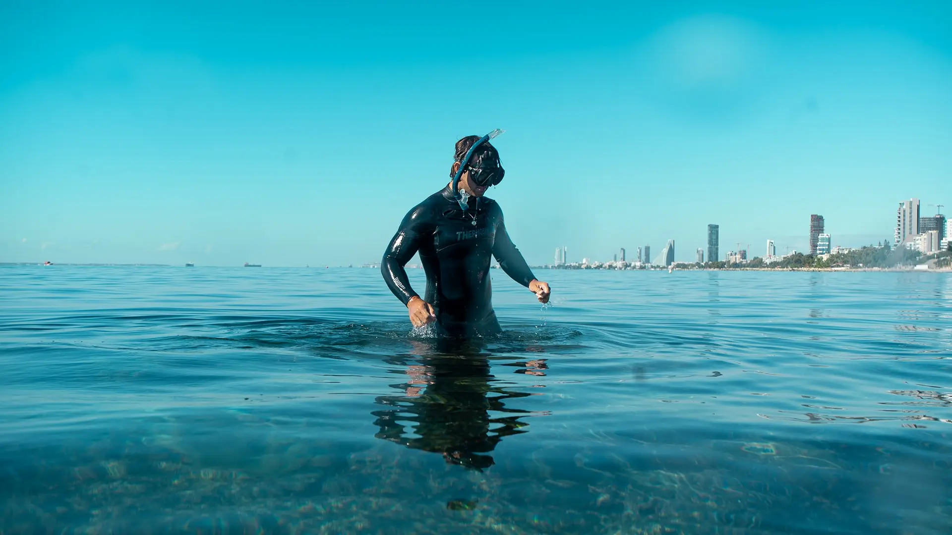Buceador con máscara de pie en el mar, con la ciudad al fondo
