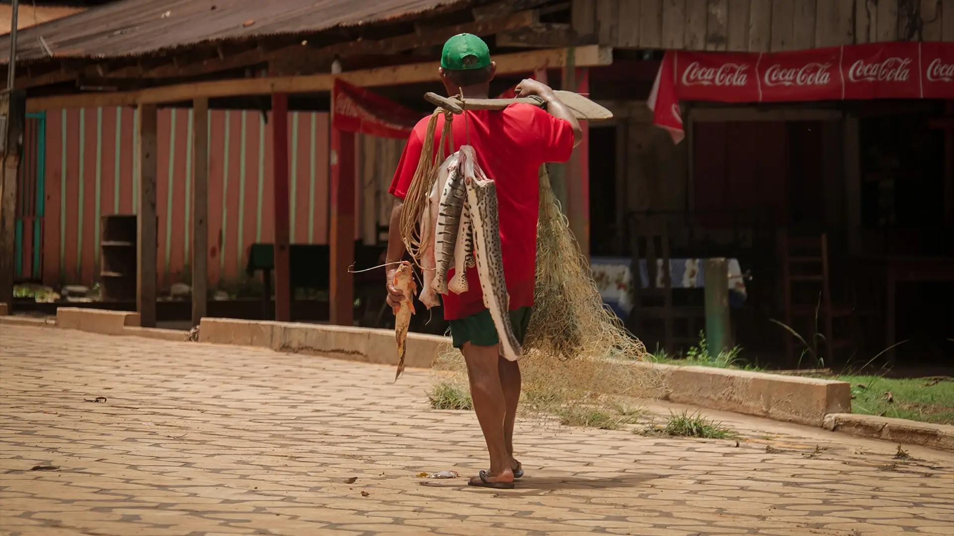 Pescador cargando su captura frente a un bar de madera