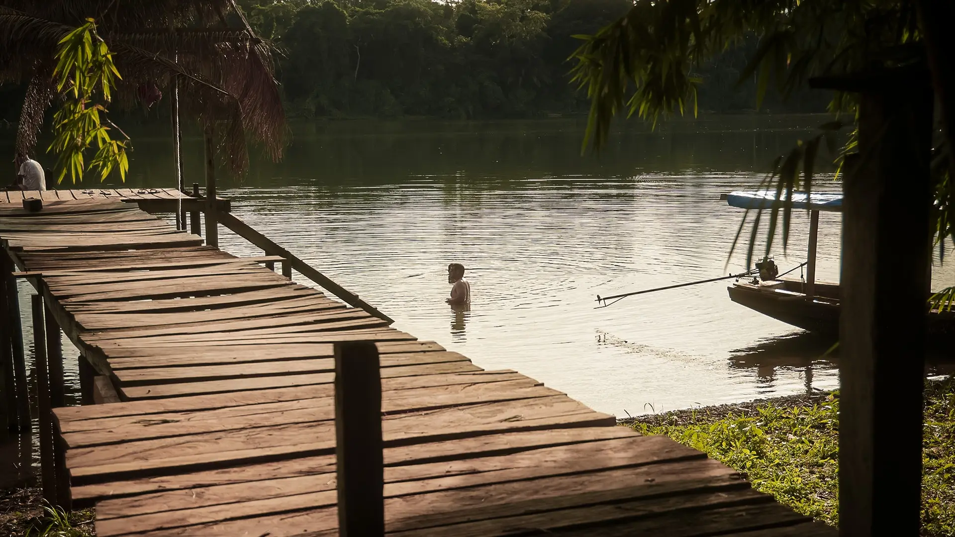 Muelle de madera que entra en el río, con un bañista al fondo